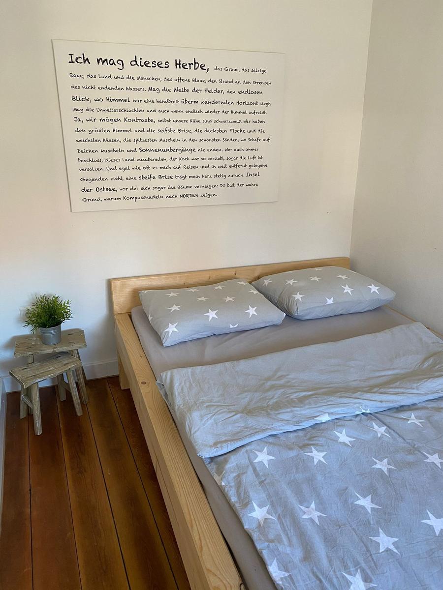 Ein Bett mit Sternenbezug, Holzrahmen und Wandtext über Ostsee.