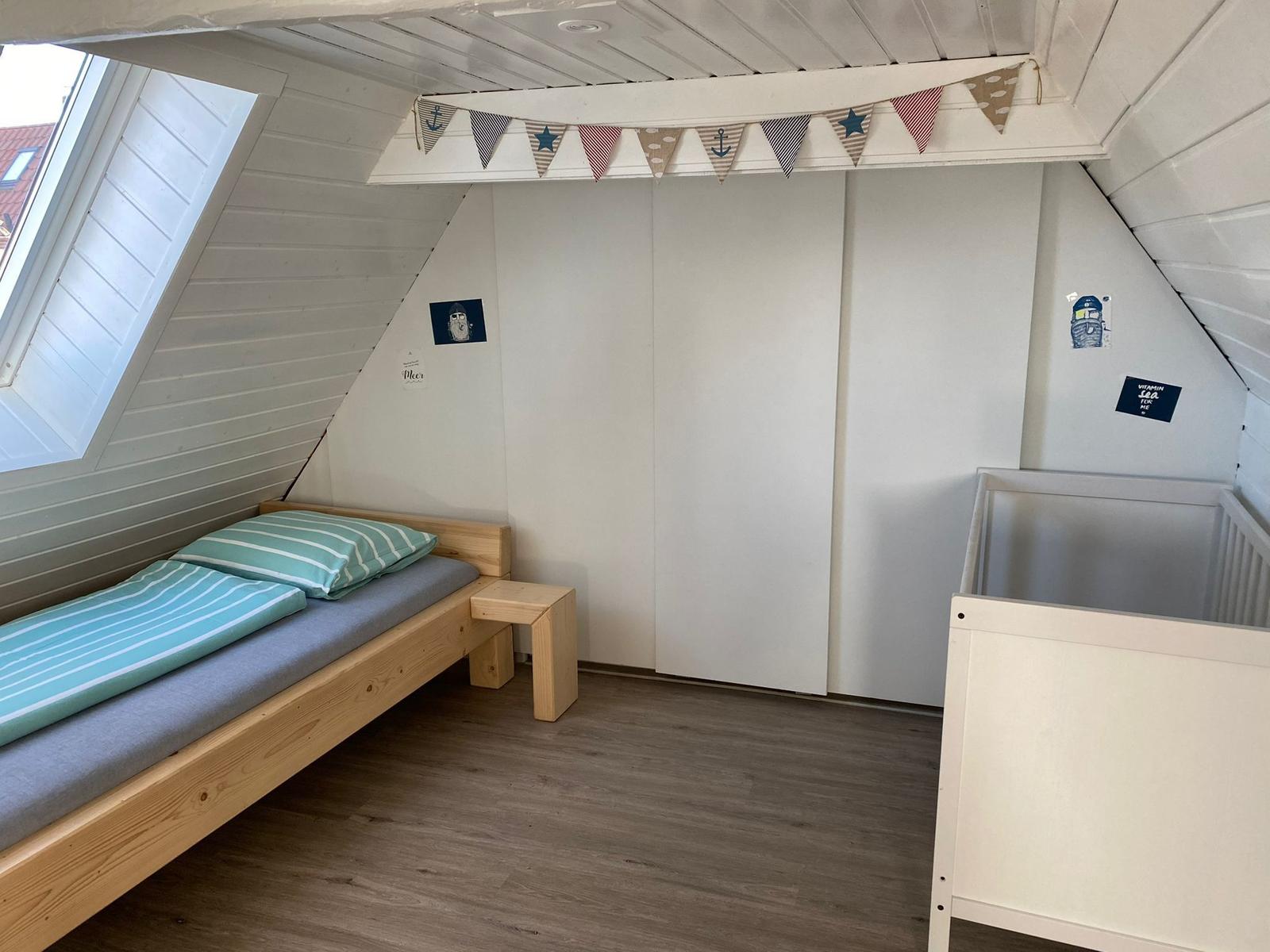 Kinderzimmer mit Bett, Kinderbett und Fenster unter Dachschrägen.