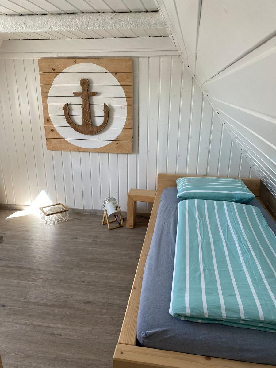 Ein Bett mit gestreifter Bettwäsche, Wanddekoration mit Anker und Holzmöbel.