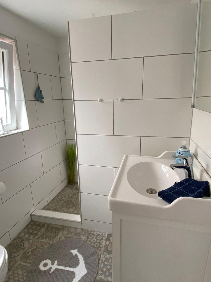 Badezimmer mit Dusche, Waschbecken und Fenster. Bodenfliesen und Wandfliesen.