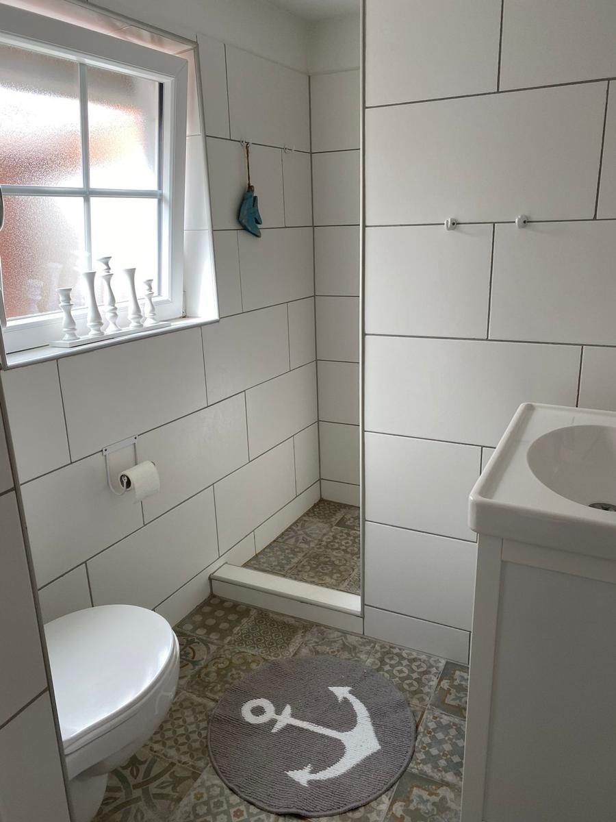 Badezimmer mit Toilette, Waschbecken und Dusche. Bodenfliesen und Wandfliesen sind weiß.