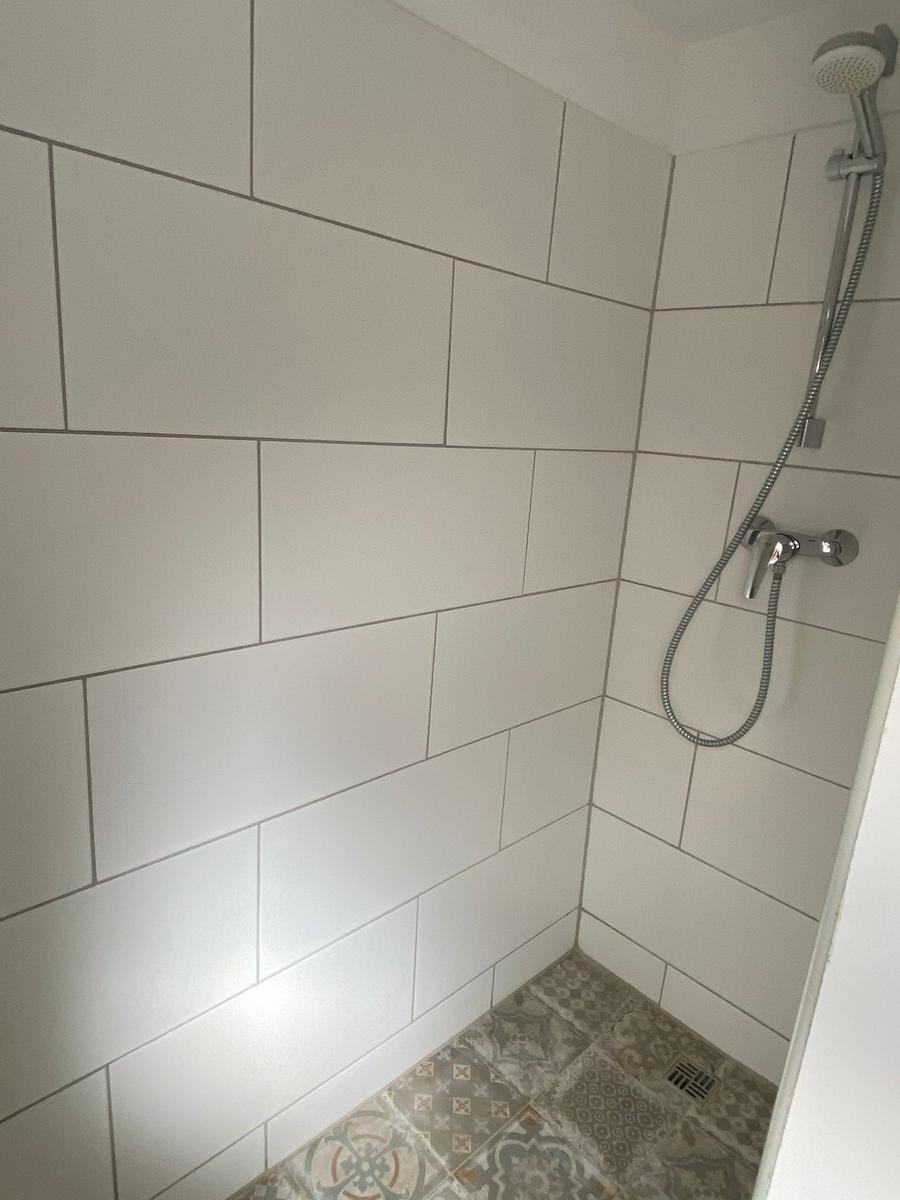 Dusche mit weißen Fliesen und dekorativem Bodenbelag