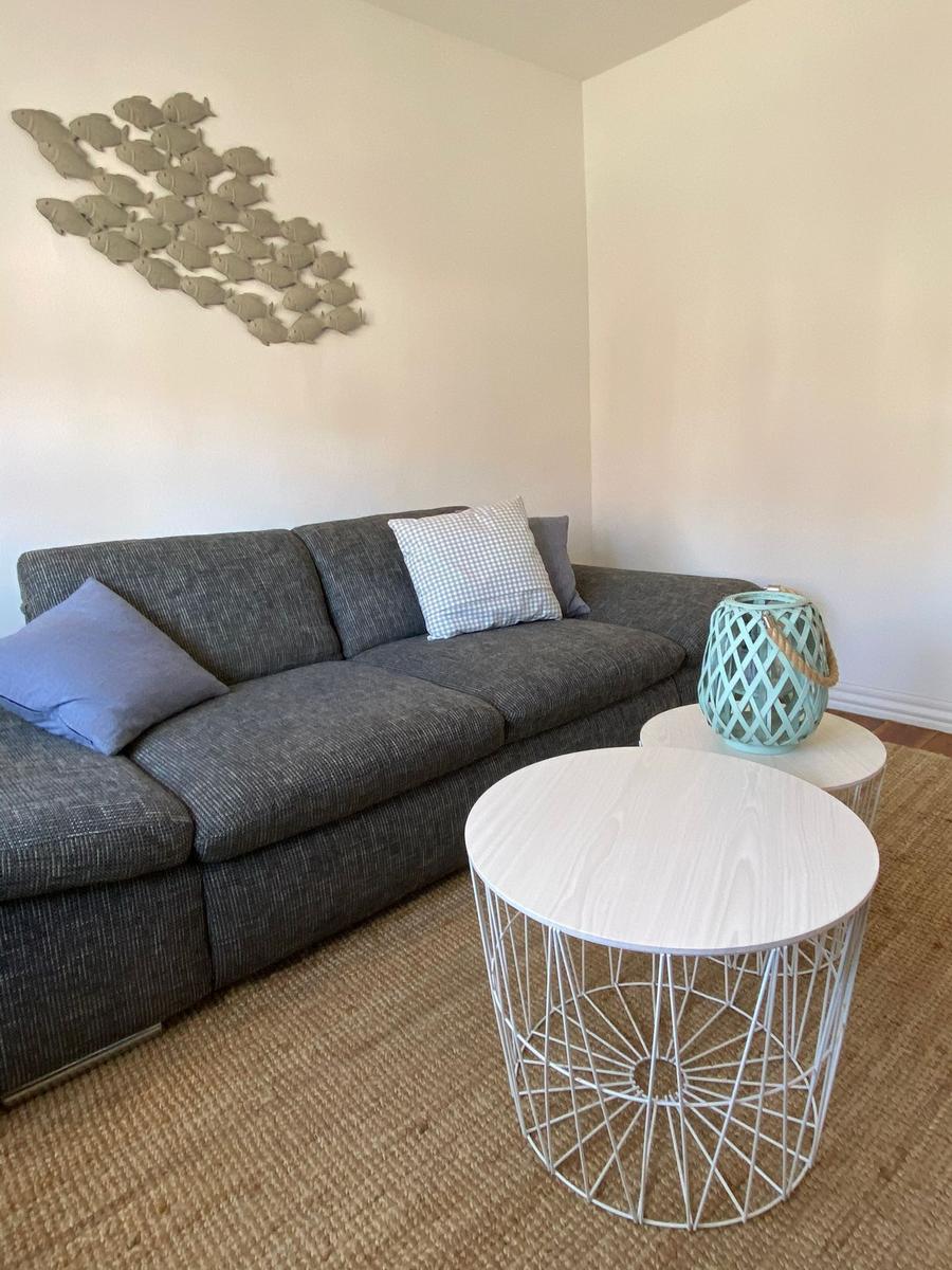 Ein grauer Sofa mit Kissen, zwei runde Tische und Wanddekoration mit Fischen.