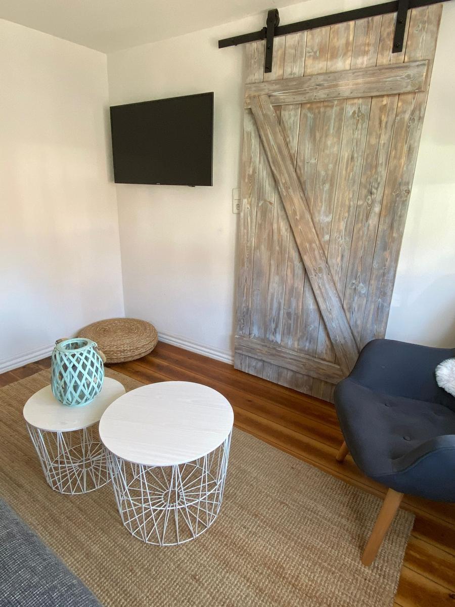 Raum mit Holztür, TV, zwei runden Tischen und Sitzgelegenheit.