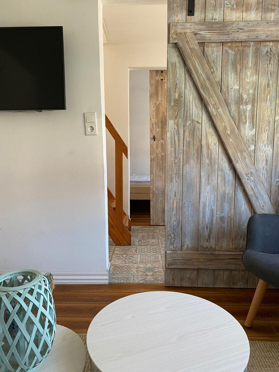 Wohnbereich mit Holztür, Fernseher und Tisch. Treppenhaus führt zur Schlafstube.