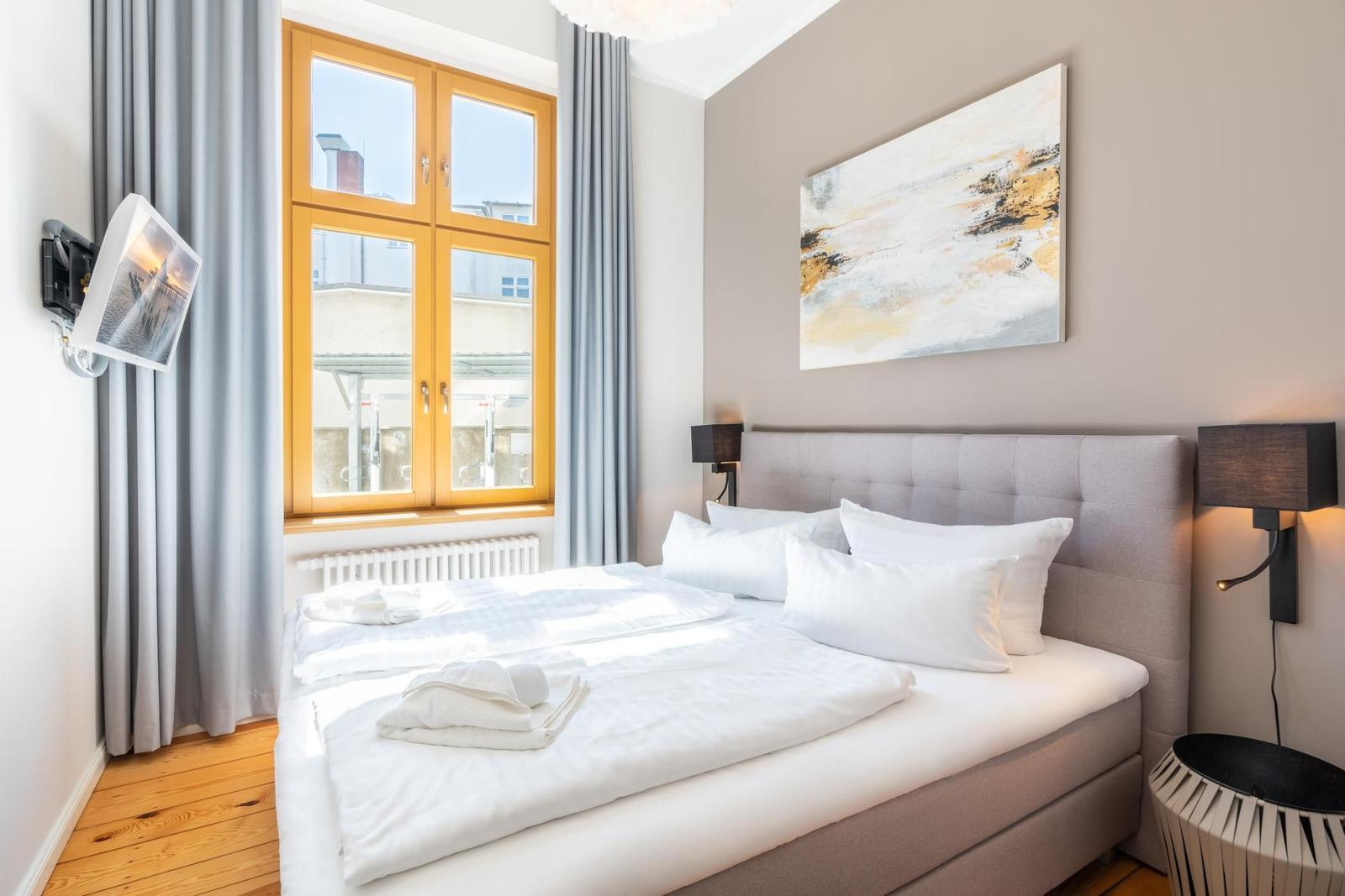 Schlafzimmer mit Bett, Fenster und Wandbild. TV an der Wand.