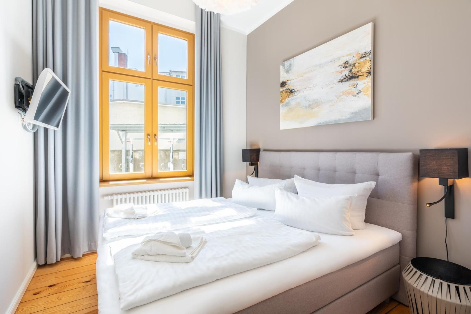Schlafzimmer mit Doppelbett, Wandbild und Fenster mit Holzrahmen.