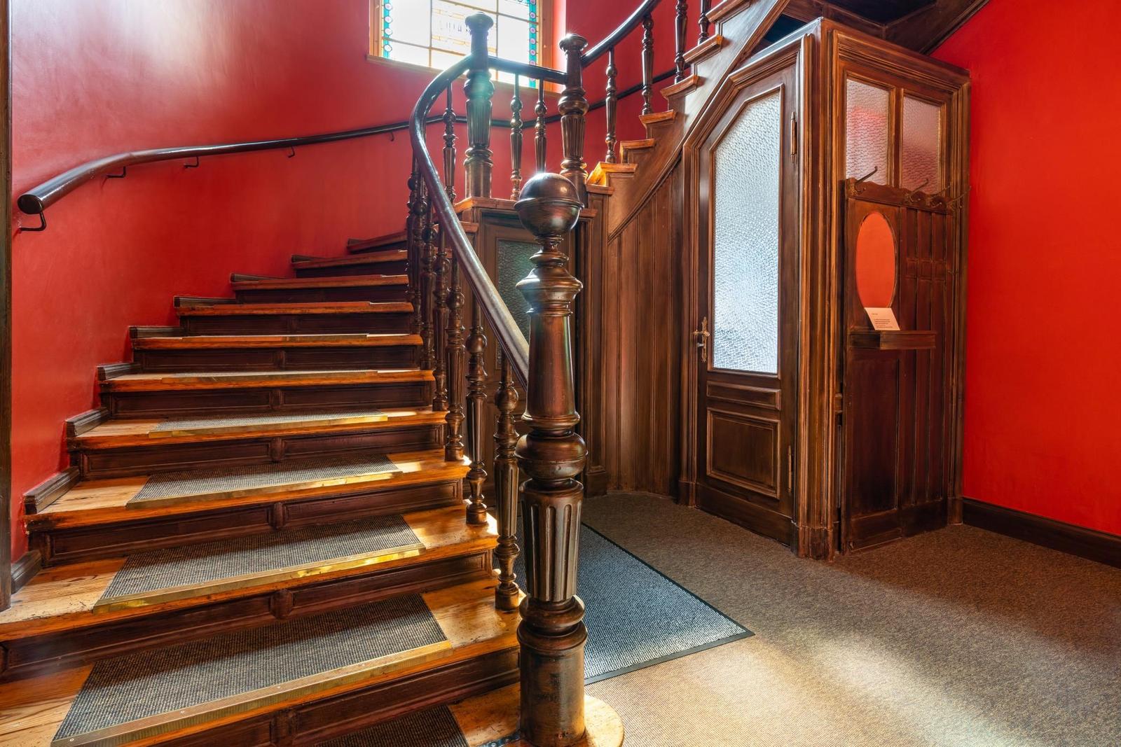 Haus mit Holztreppe, roten Wänden und Holzgeländer. Tür mit Glasfenster und Teppichboden.