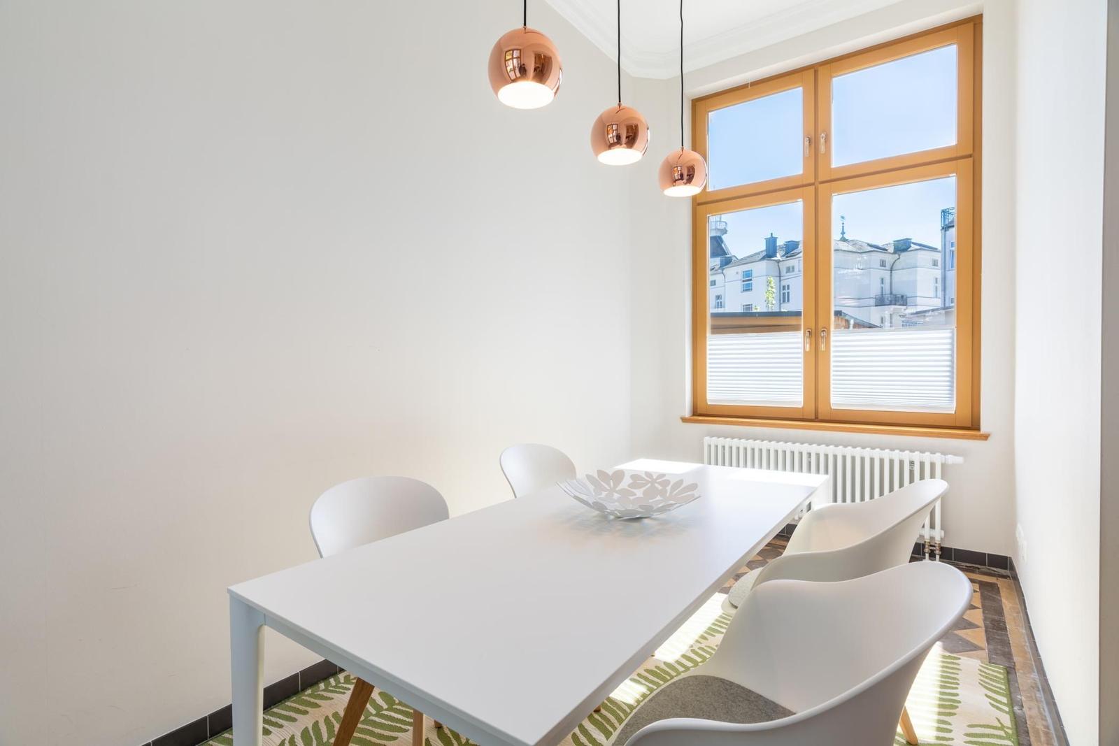 Esszimmer mit weißem Tisch, weißen Stühlen und drei kupferfarbenen Hängelampen an der Wand.