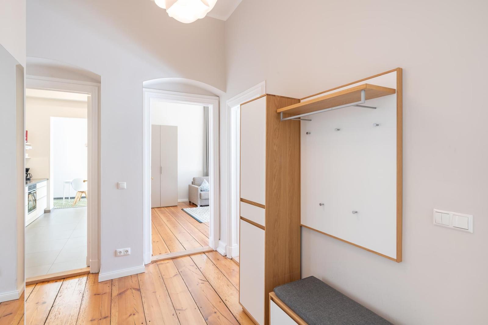 Flur mit Holzboden, Kleiderschrank und Blick in Küche und Wohnzimmer.