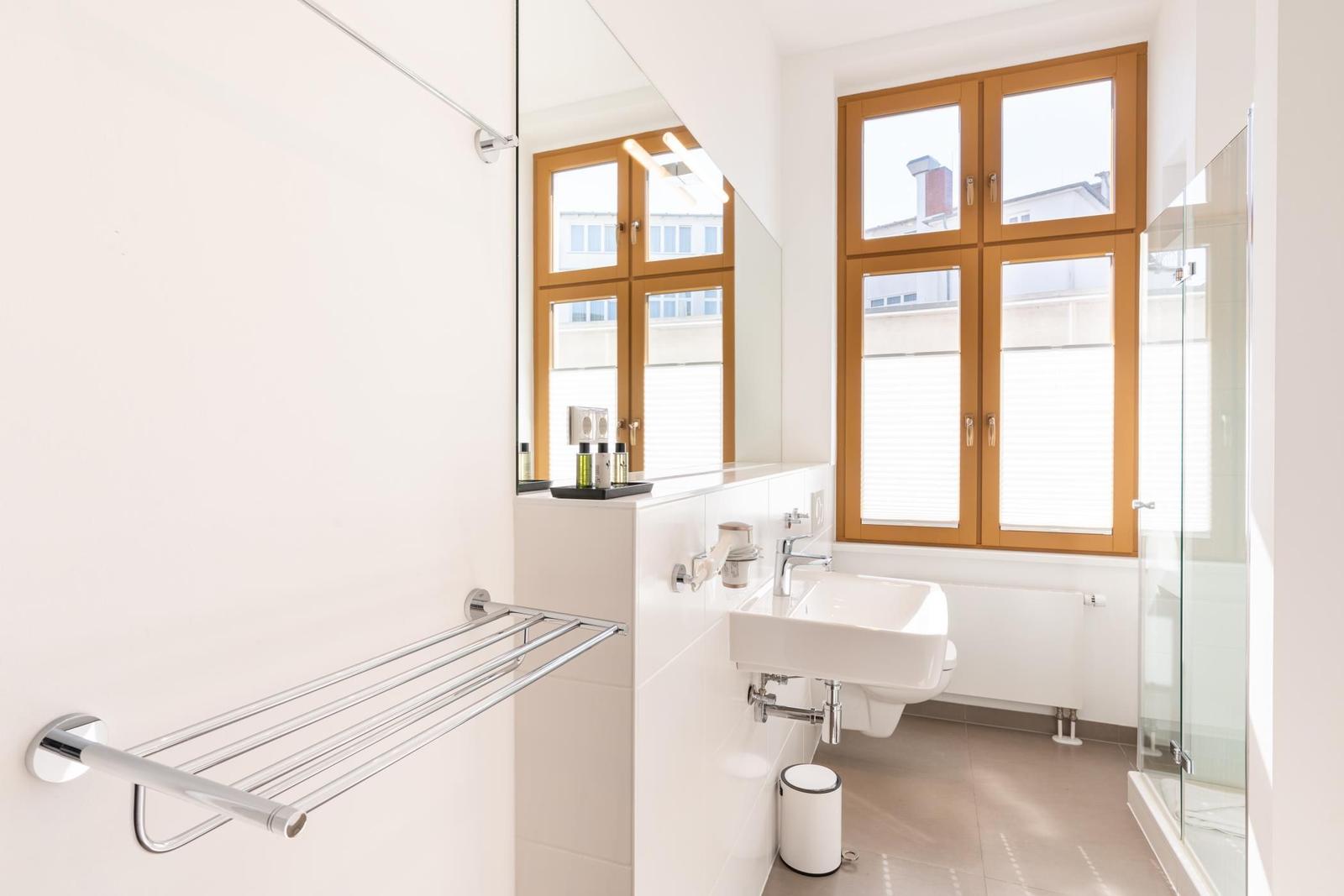 Badezimmer mit Waschbecken, Spiegel, Dusche und Fenster mit Holzrahmen.