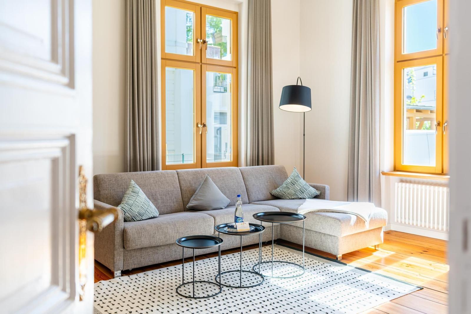 Ein Wohnzimmer mit Sofa, zwei Tischen und Fenstern mit Vorhängen.