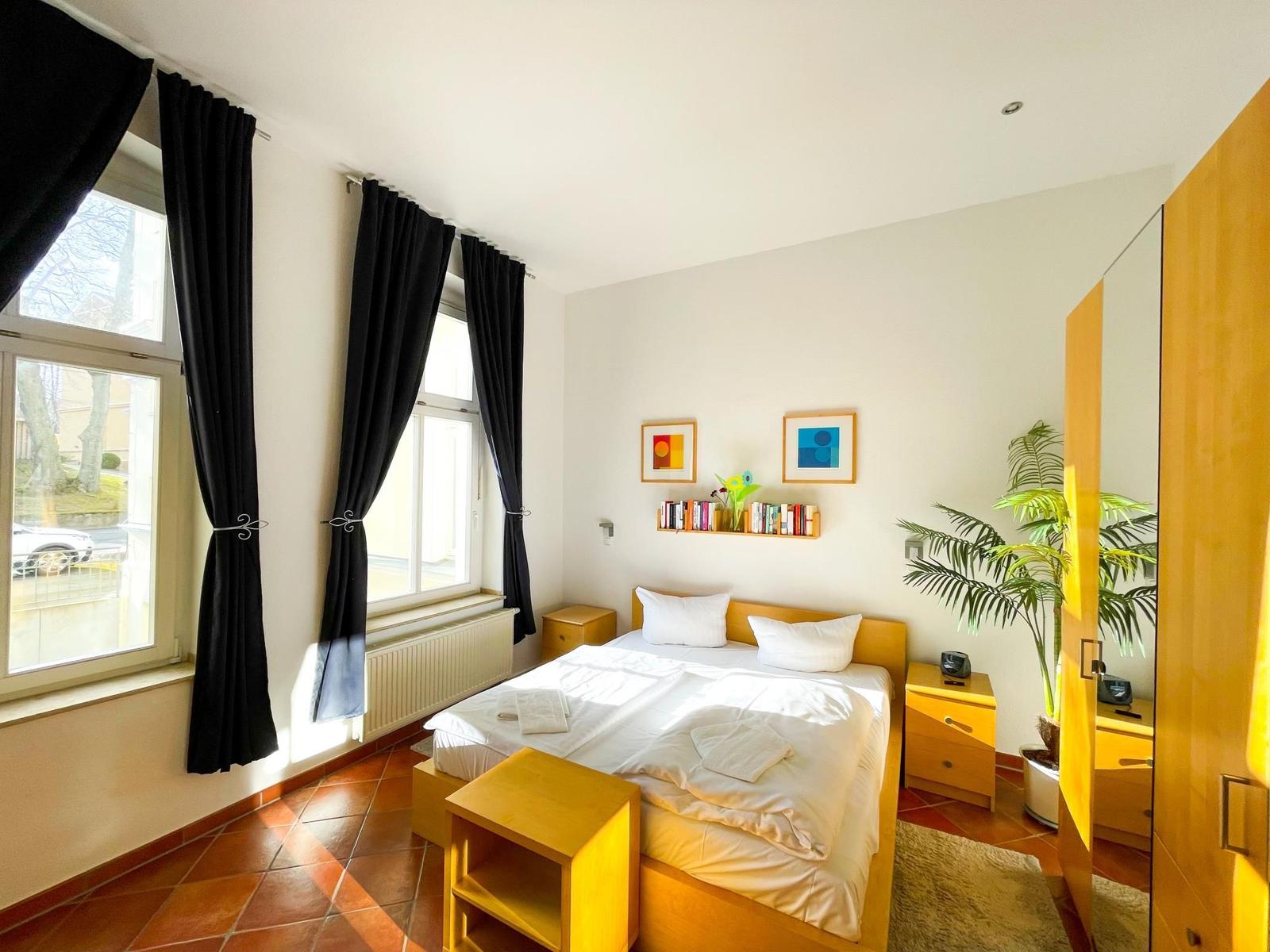 Schlafzimmer mit Doppelbett, Fenstern, Schränken und Pflanze.
