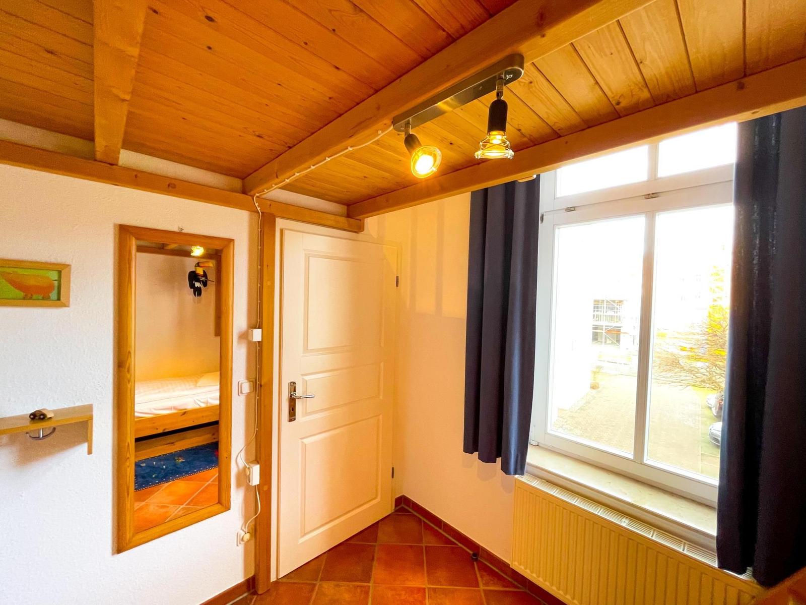 Raum mit Holzdecke, Fenster, Tür und Blick in Schlafzimmer.