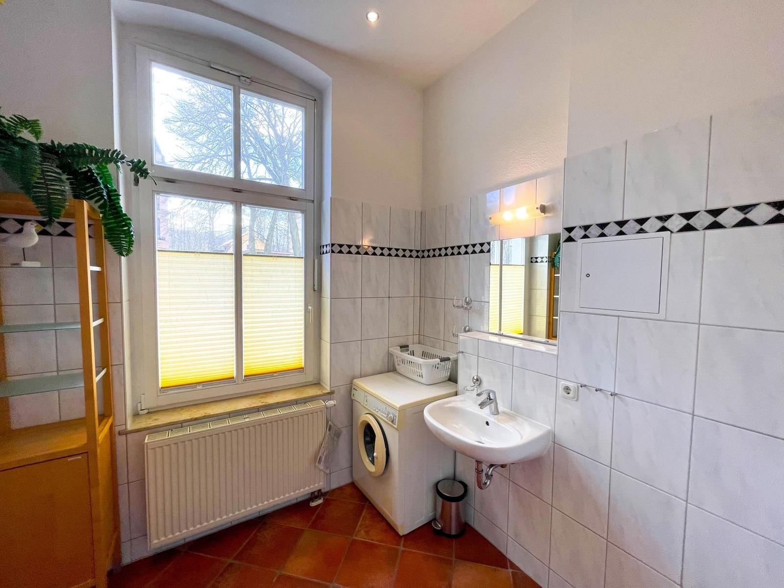 Badezimmer mit Waschmaschine, Waschbecken und Fenster mit Jalousie.