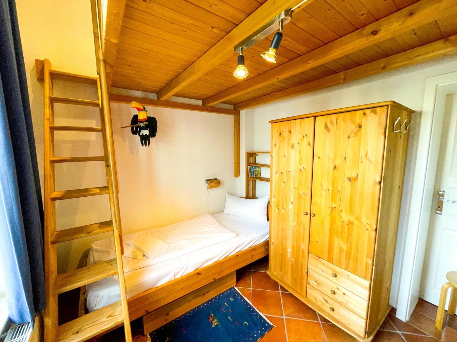 Ein Schlafzimmer mit Holzbett, Kleiderschrank und Decke. An der Wand hängt ein Vogel.