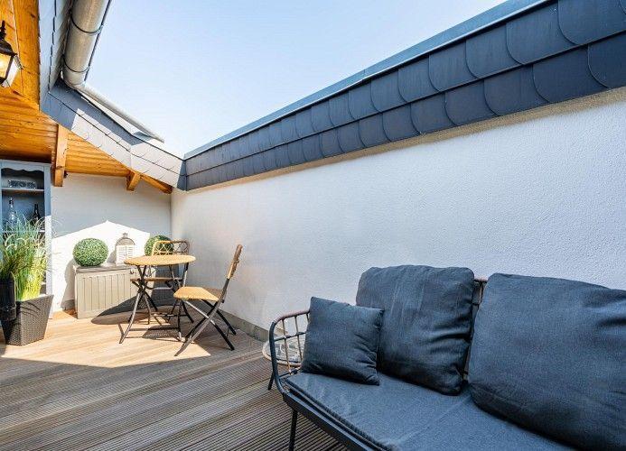 Terrasse mit Sitzgelegenheit, Tisch, Stühlen und Pflanzen unter Dach