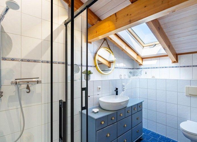 Badezimmer mit Dusche, Waschbecken und Toilette unter Holzbalkendecke mit Dachfenster.