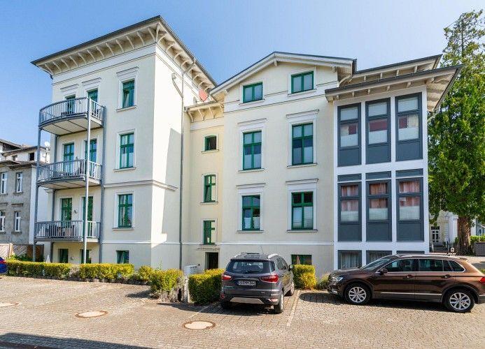 Fünfgeschossiges Gebäude mit Balkonen und Fenstern. Zwei Autos parken vor dem Haus.