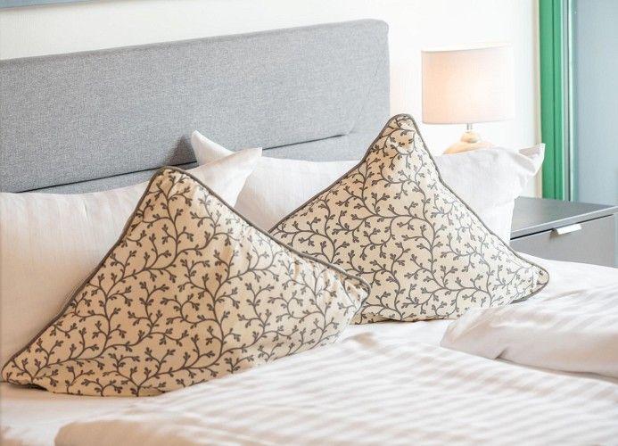 Doppelbett mit Kissen und Nachttisch. Lampe und grüner Rahmen sichtbar.