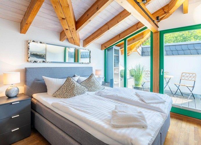 Schlafzimmer mit Doppelbett, Holzbalkendecke und Glasfront zur Terrasse.
