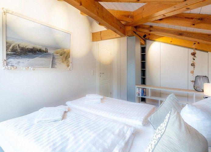 Schlafzimmer mit Doppelbett, Holzbalkendecke und Wandbild mit Strandmotiv.