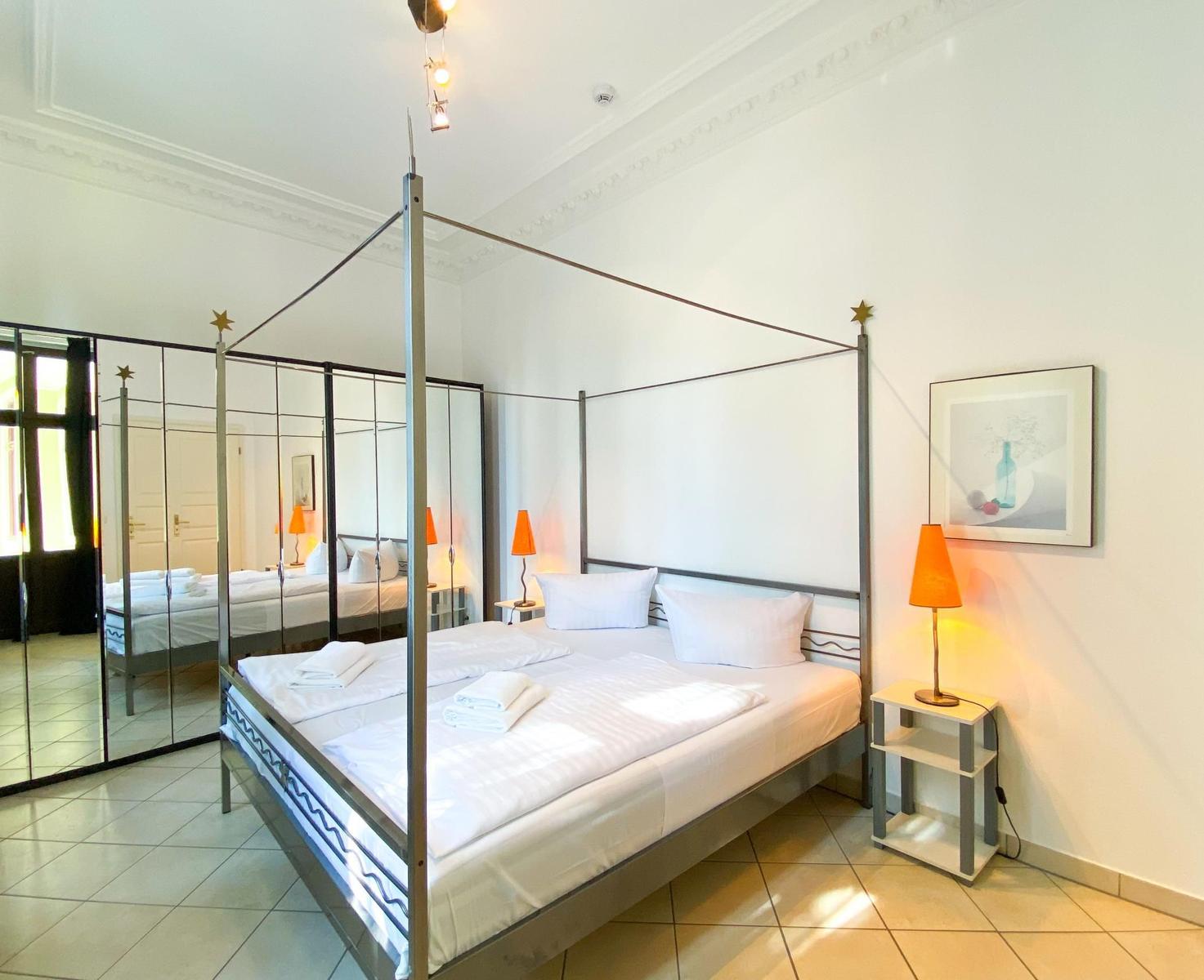 Schlafzimmer mit Doppelbett, Spiegelschrank und Nachttisch mit Lampe.