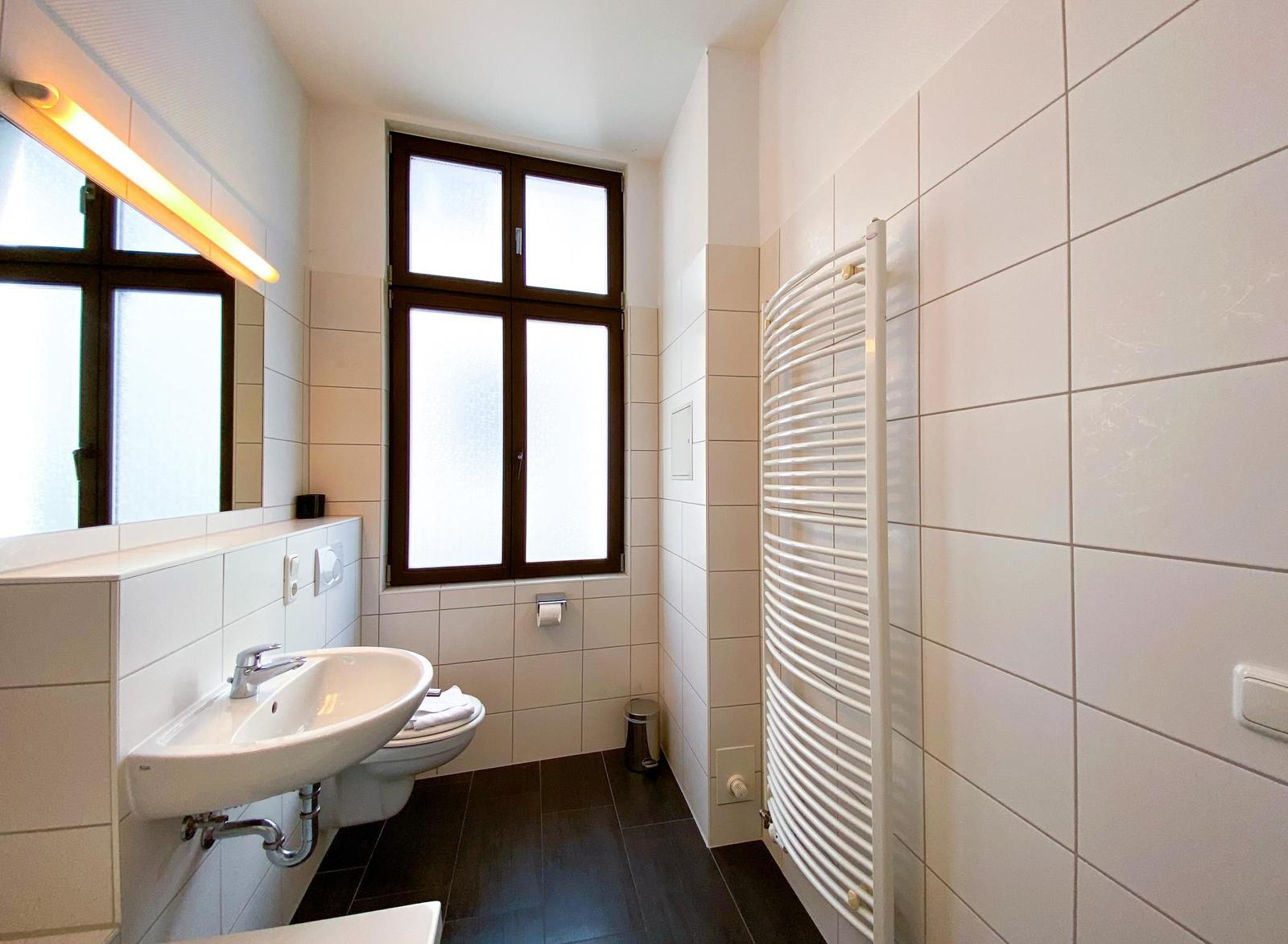 Badezimmer mit Waschbecken, Toilette, Heizung und Fenster.