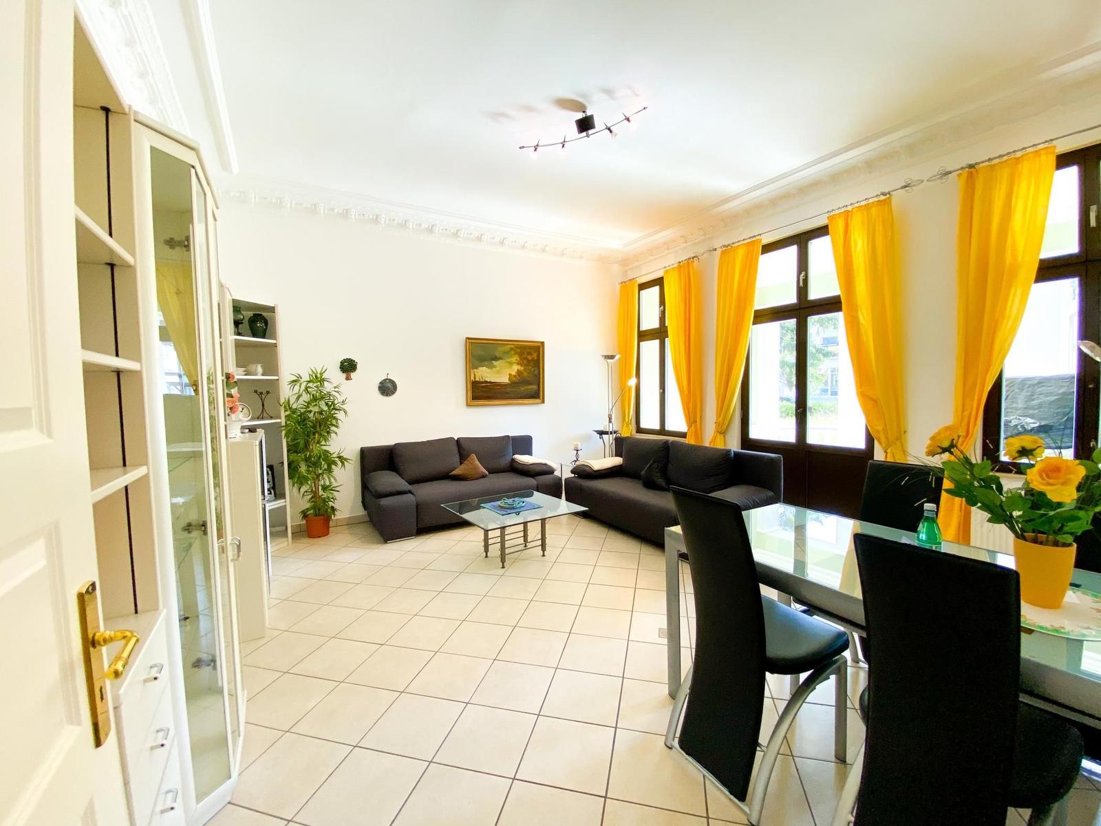 Wohn- und Essbereich mit Sofa, Tisch und gelben Vorhängen.