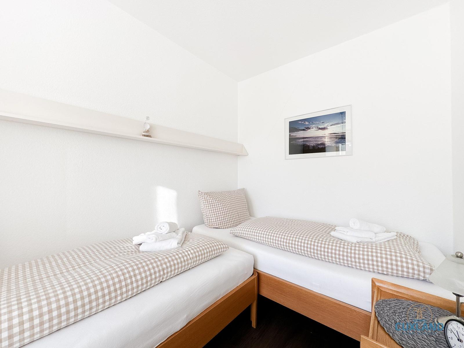Zwei Einzelbetten mit karierten Bettwäsche, Wandbild und Nachttisch mit Wecker.