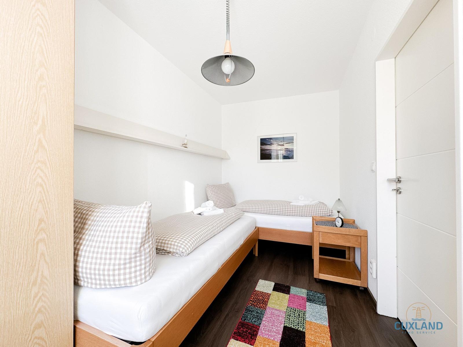 Zwei Einzelbetten mit Kissen und Bettwäsche. Holzfußboden, Deckenventilator und Wandbild.