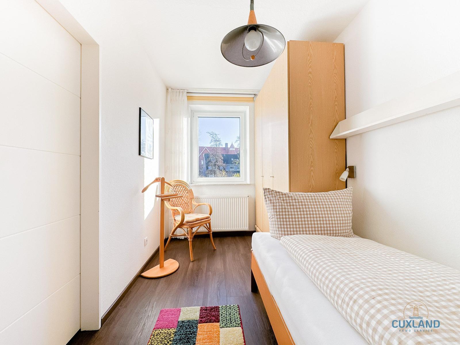 Ein Schlafzimmer mit Bett, Kleiderschrank und Stuhl vor dem Fenster.