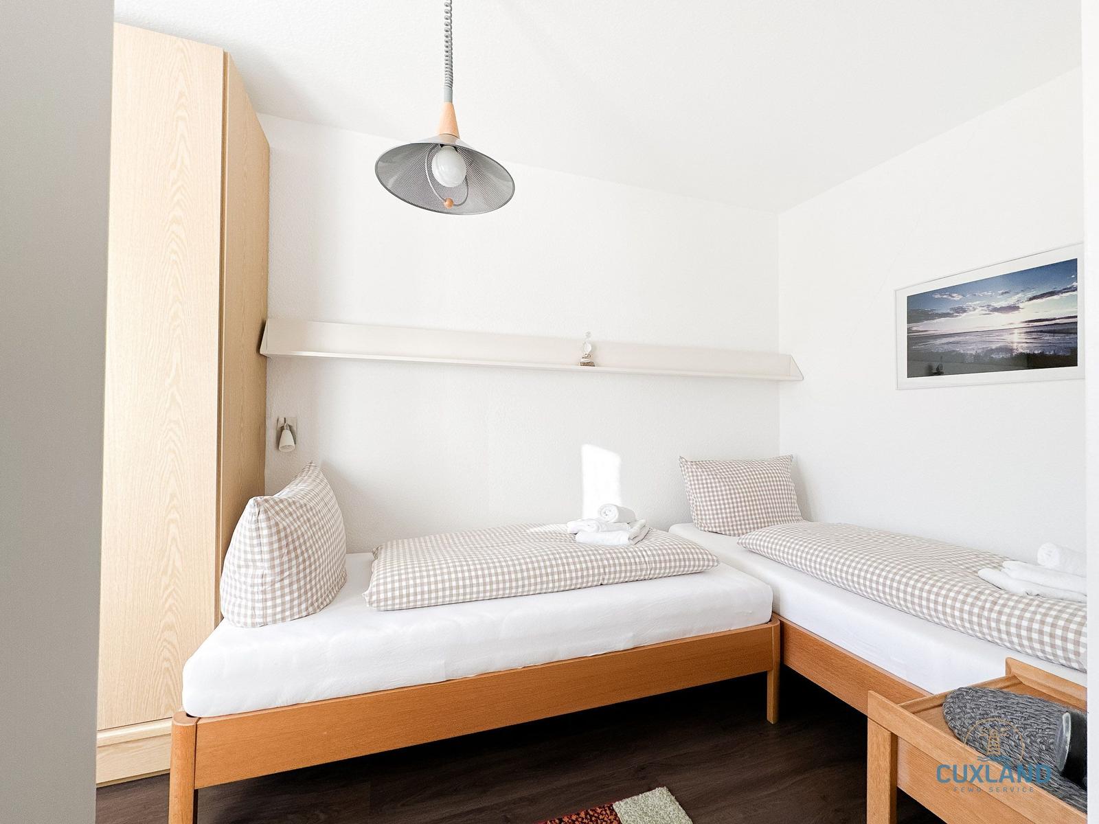 Zwei Einzelbetten mit karierten Bezügen und weißen Matratzen. Holzmöbel und Wandbild.