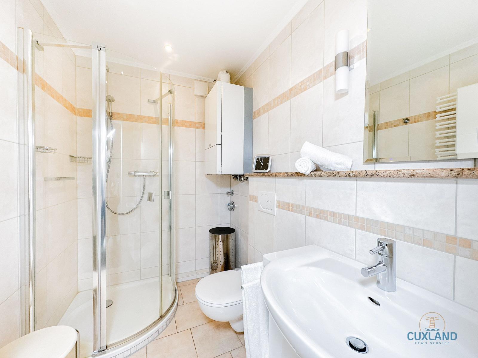 Badezimmer mit Dusche, Waschbecken und Toilette. Fliesen und Spiegel sichtbar.