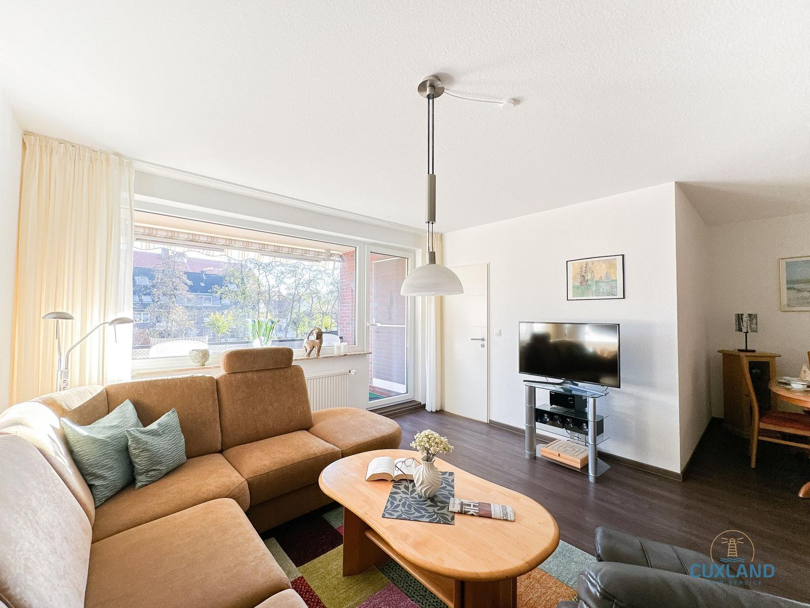 Wohnzimmer mit Sofa, Couchtisch und Fernseher. Fenster mit Blick auf Balkon.