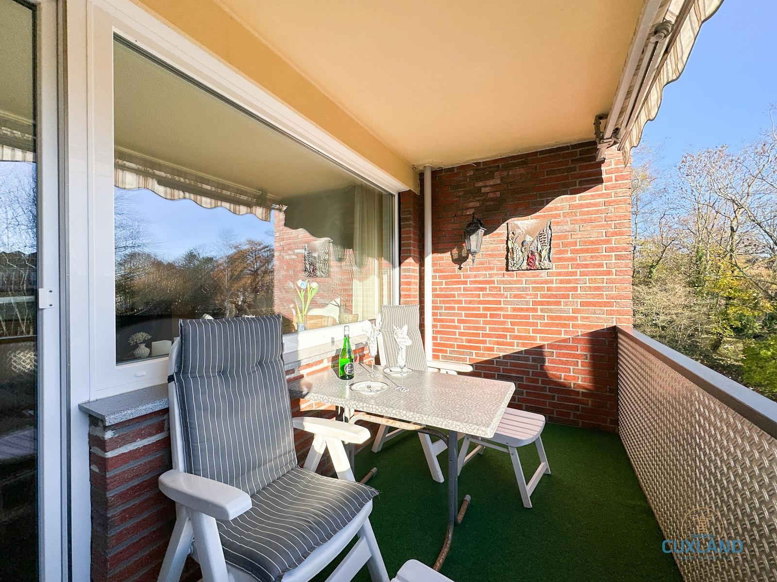 Terrasse mit Tisch, Stühlen und grünem Boden. Roter Ziegelwand und Sonnenschutz.