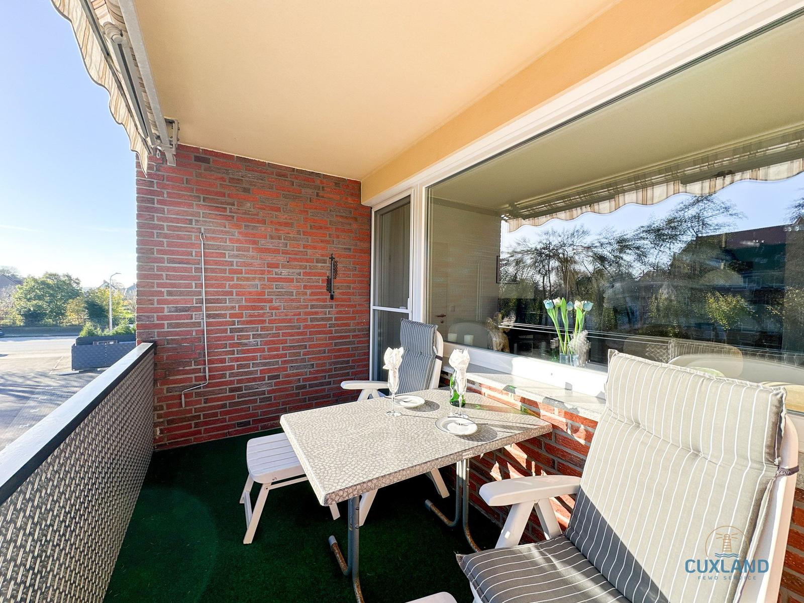 Terrasse mit Tisch, Stühlen und grünem Bodenbelag. Roter Ziegelwand und Glasfront.