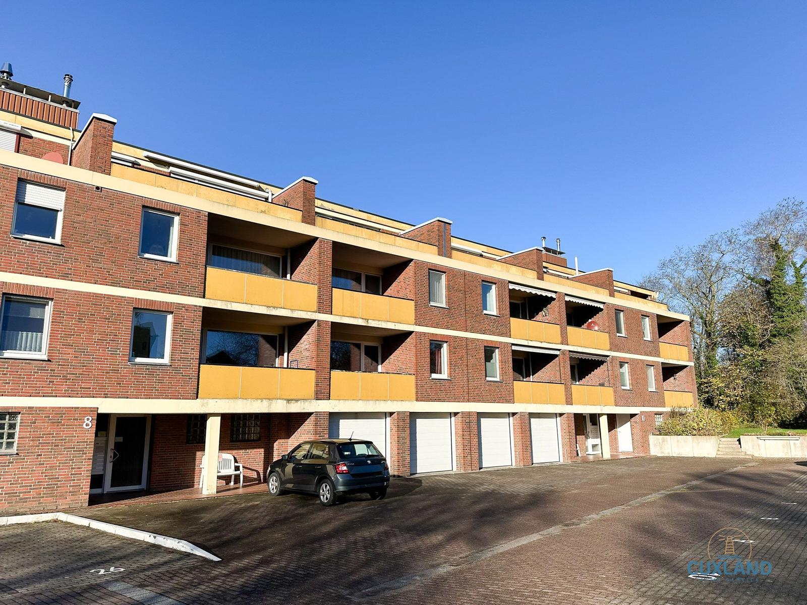 Rotes Backsteinhaus mit Balkonen und Garagen. Ein Auto steht auf dem Hof.