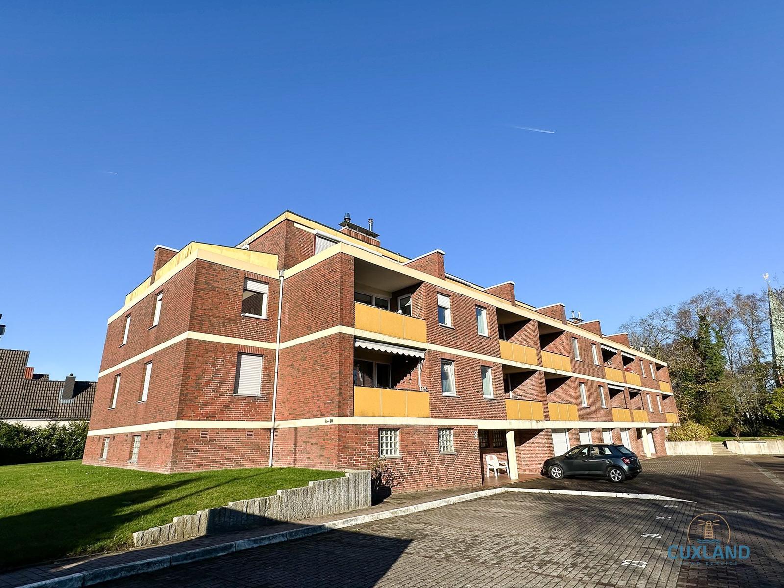 Rotes Backsteingebäude mit Balkonen und Parkplatz vor einem klaren Himmel.