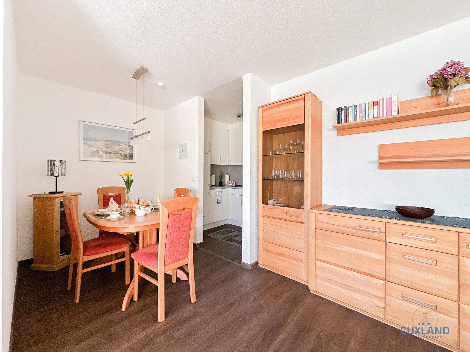 Essbereich mit Holztisch, Stühlen und Küchenbereich im Hintergrund.