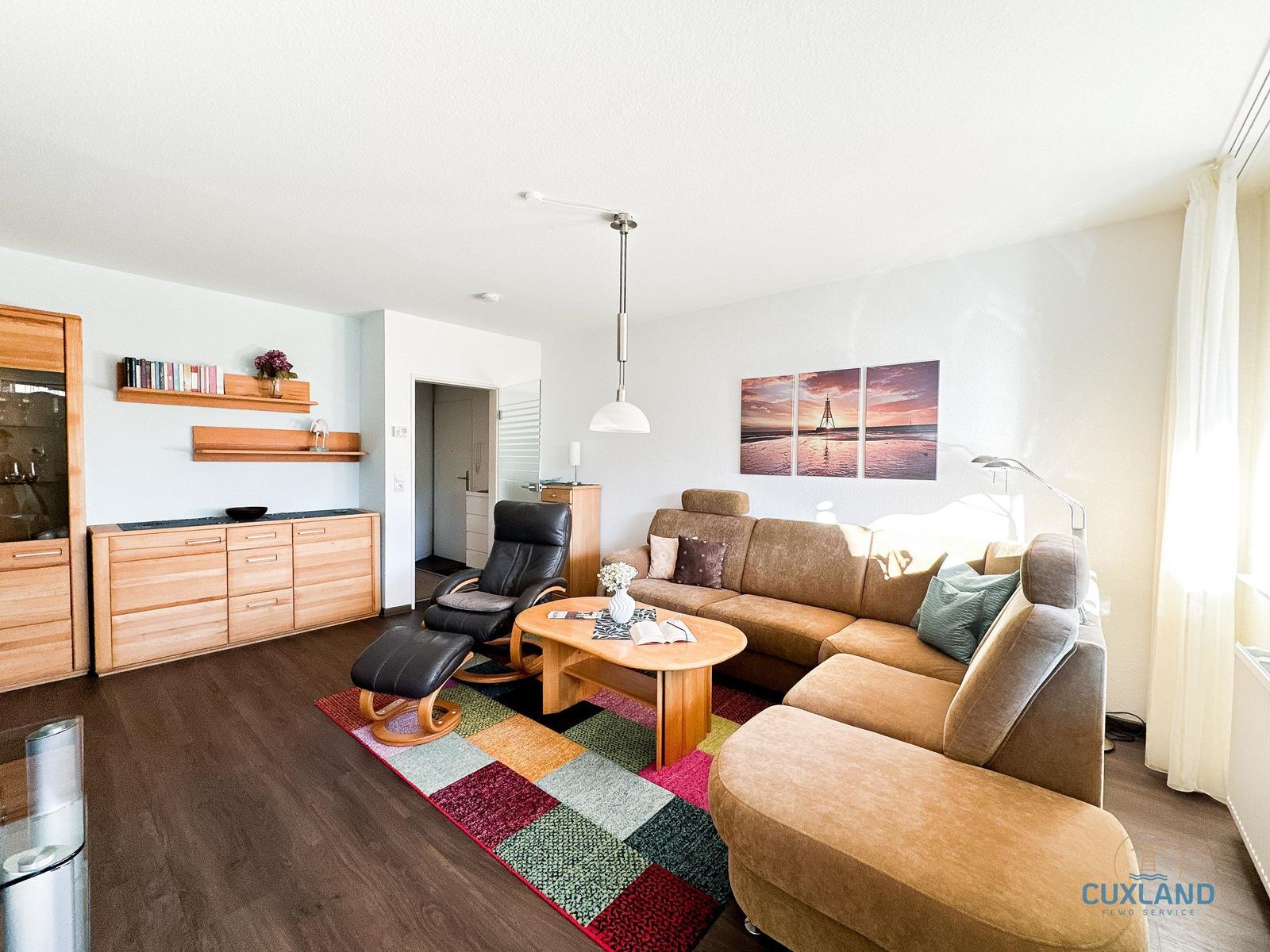 Wohnzimmer mit Sofa, Sessel und Holzmöbel. Wandbild zeigt Leuchtturm.