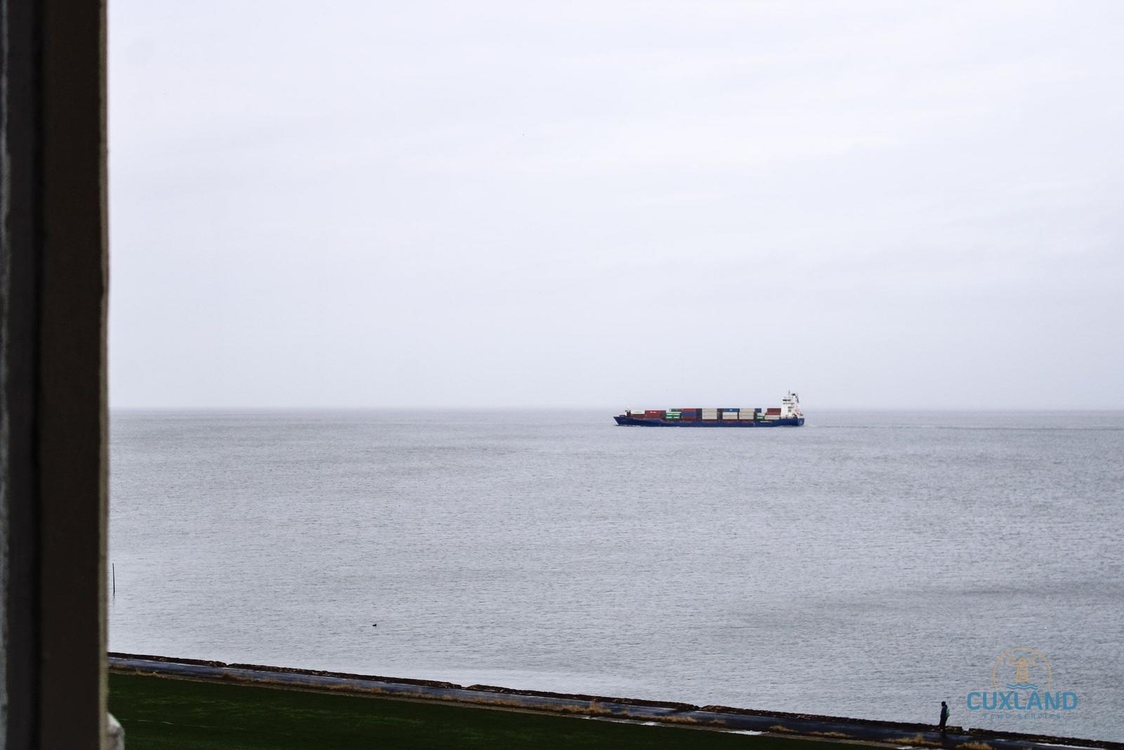 Vom Fenster aus Blick auf das Meer mit einem Containerschiff in der Ferne.