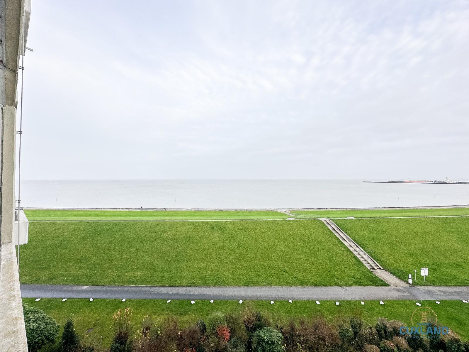 Weitläufiger Grünstreifen mit Blick auf Meer und Hafenbecken.