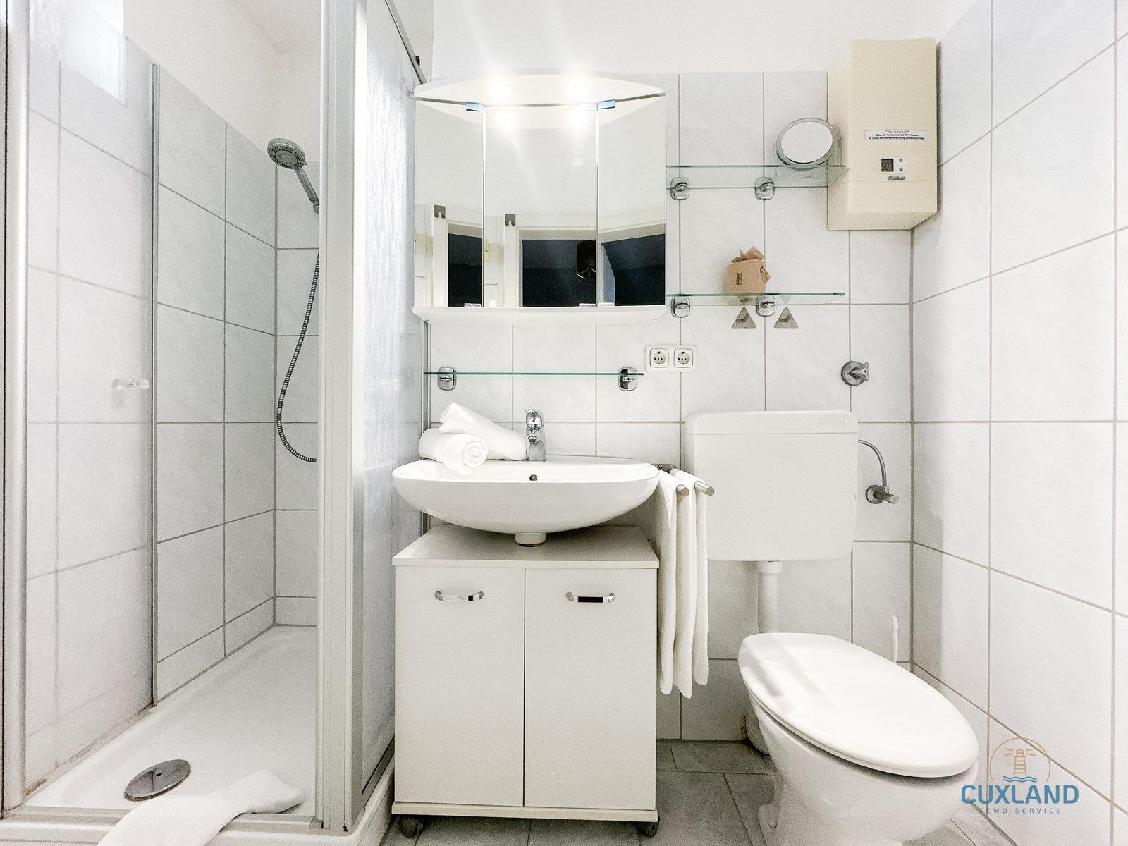 Badezimmer mit Dusche, Waschbecken und Toilette. Weiße Fliesen und Spiegelschrank.