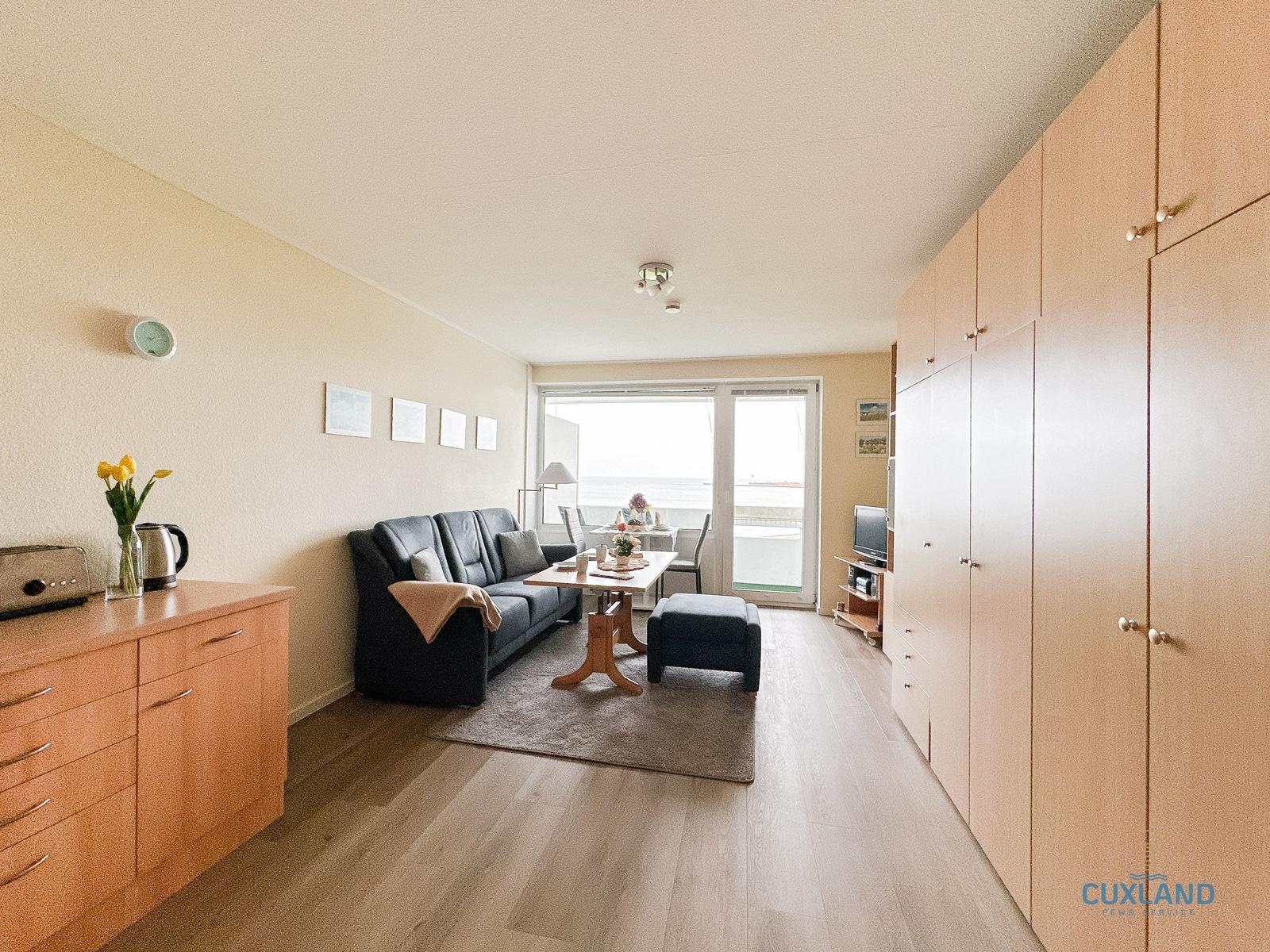Wohnzimmer mit Sofa, Esstisch und Balkon. Holzoberflächen und große Schränke.