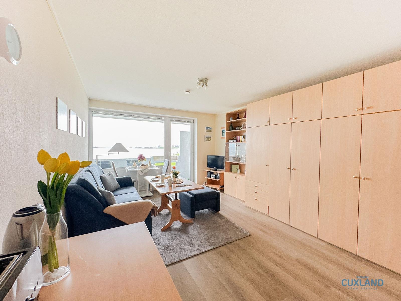 Wohnbereich mit Sofa, Esstisch und großen Schränken. Fenster mit Blick auf Wasser.