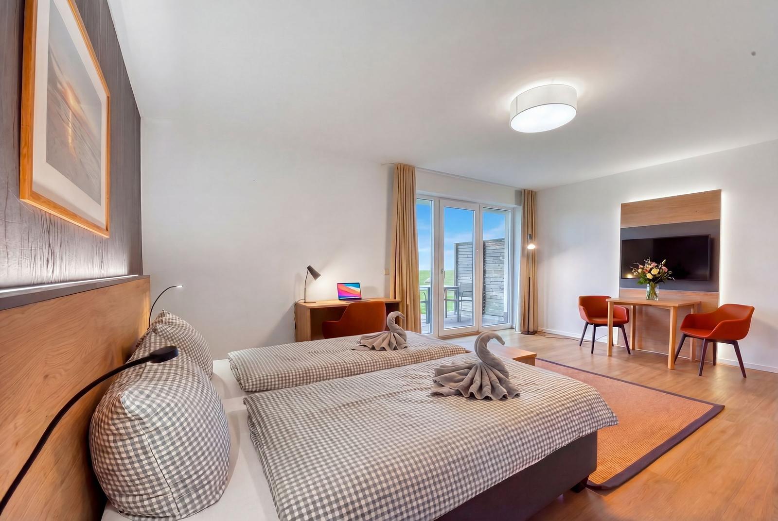 Zwei Betten mit Handtüchern als Schwäne, Schreibtisch, Fernseher und Balkon mit Sicht auf Grün.