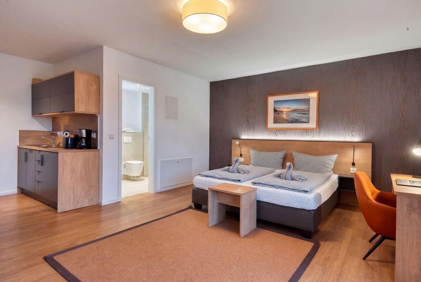 Zimmer mit Bett, Schreibtisch, Bad und Küchenbereich.