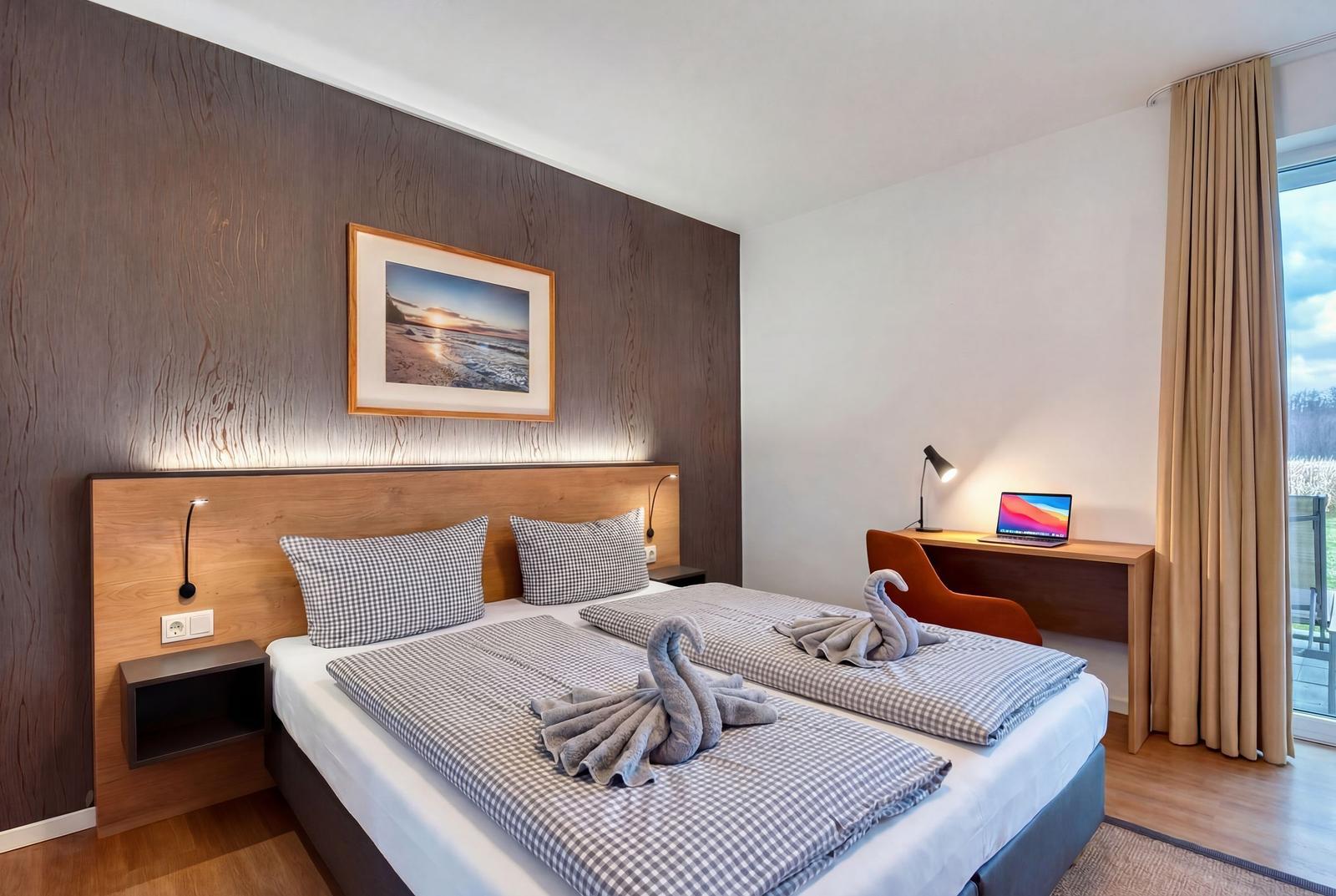 Doppelbett mit Schwänen aus Handtüchern, Schreibtisch und Blick auf Balkon.