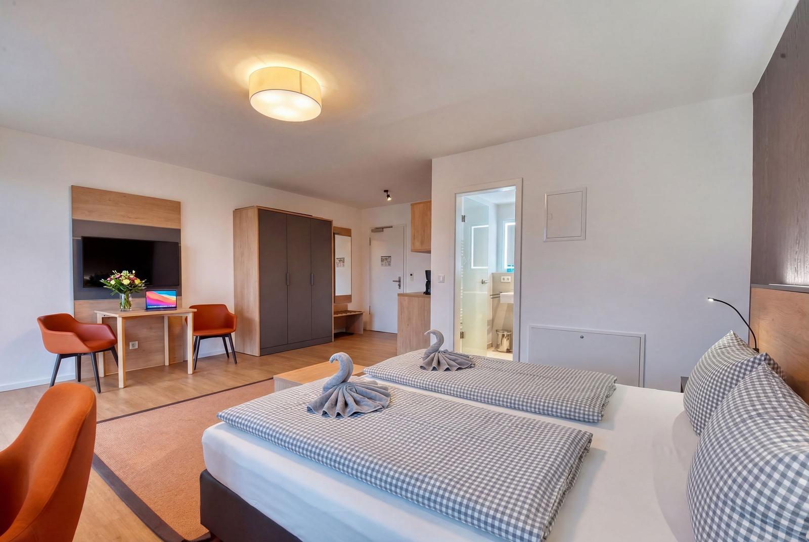 Zimmer mit Doppelbett, Schreibtisch, Kleiderschrank und Bad. Handtücher als Schwäne dekoriert.